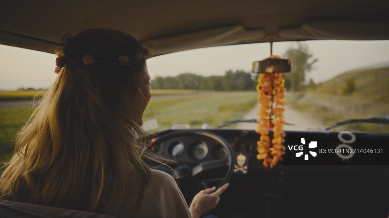 年轻女性在乡间公路上驾驶复古面包车，夕阳西下。图片素材