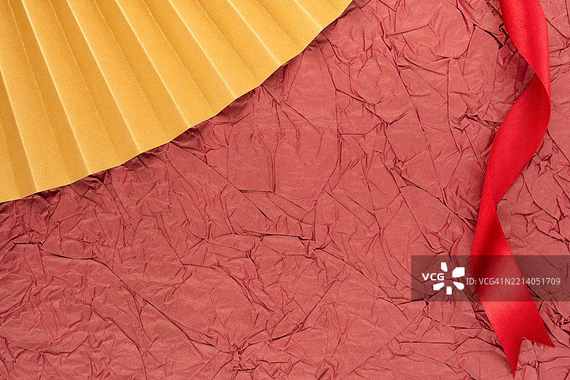 金色折纸和红色丝带在红色背景上，留有空白位置。图片素材