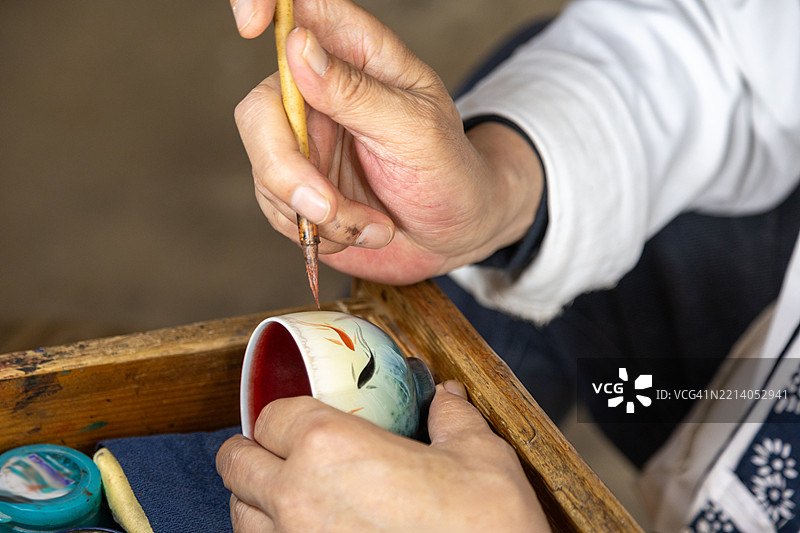 工人在中国景德镇的一家陶瓷工厂装饰瓷杯。图片素材