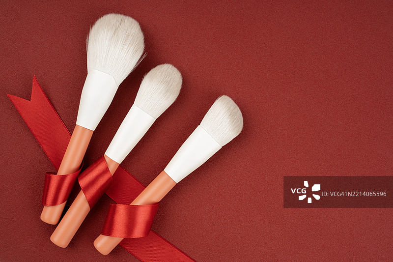 红色背景上的化妆刷和红色缎带，平铺布局，留有空白。图片素材