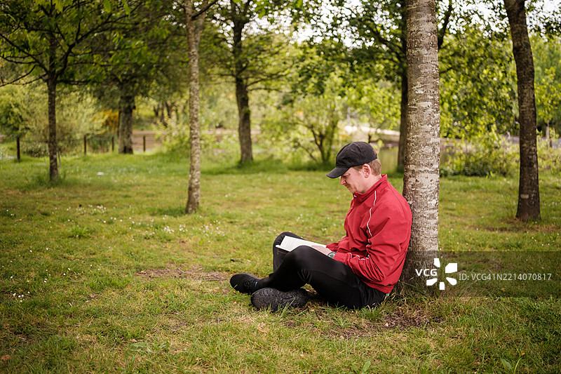 男人在宁静的公园里树下阅读一本书图片素材