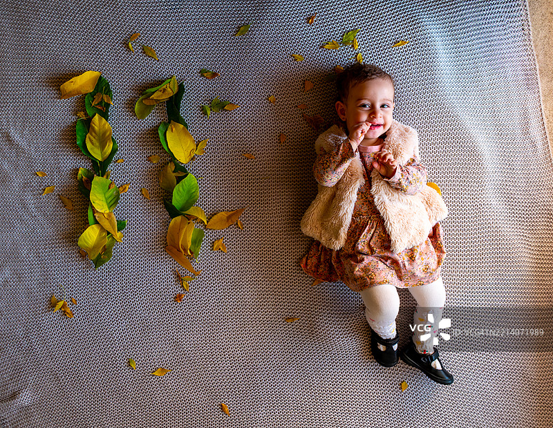 可爱的宝宝在灰色羊毛上玩耍，周围是五彩缤纷的叶子排列。图片素材