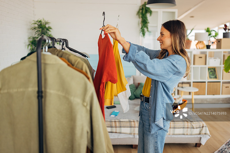 一位可爱的女性站在衣架旁，正在挑选旅行要带的衣物。图片素材