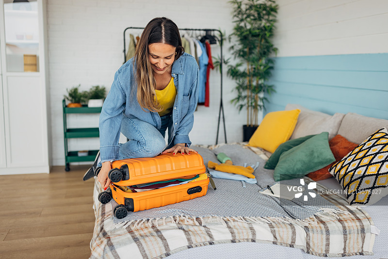 微笑的女人在床上合上行李箱，兴奋地为即将到来的假期做准备，充满了快乐和对即将到来的冒险的期待。图片素材