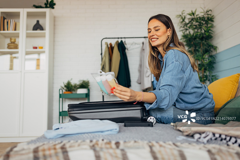 女人在家里的床上把衣服装进行李箱，微笑着享受整理行李的过程，为一次激动人心的旅行做准备。图片素材