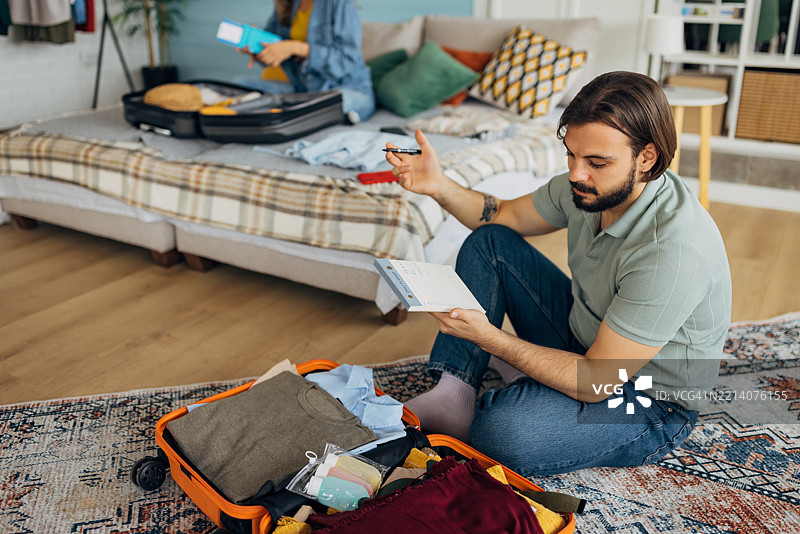 一对男女在卧室里收拾行李，为旅行做准备，享受周末活动。图片素材