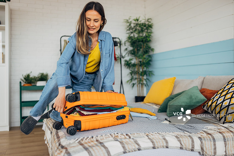 女人用膝盖试图合上一个装满的行李箱图片素材