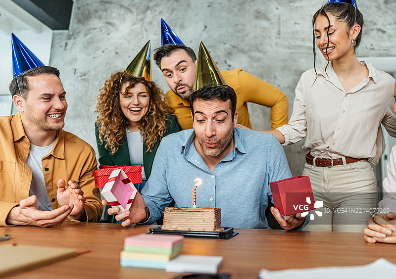 商人在同事的庆祝下吹灭生日蛋糕上的蜡烛图片素材