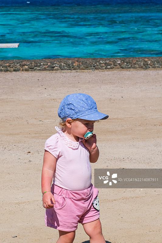 一个小女孩站在海滩上，穿着粉色的衬衫和粉色的裙子。图片素材