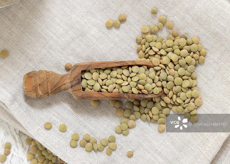 木制勺子盛满干燥的绿色扁豆，放在米色餐巾上，俯视图，传统地中海豆类。图片素材
