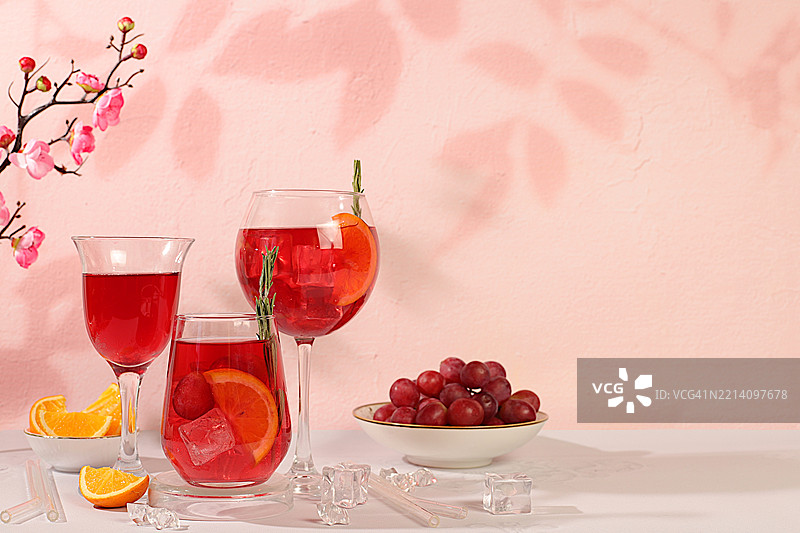 优雅的桌子上摆放着葡萄鸡尾酒、红酒和葡萄汁，配有葡萄浆果、冰块和柑橘片。图片素材