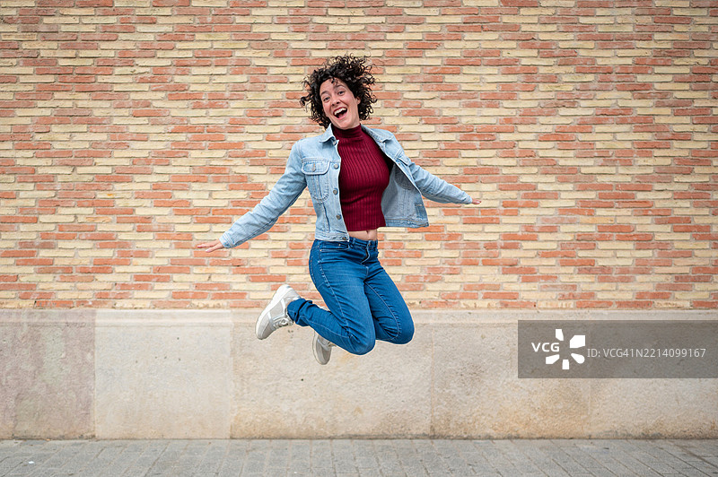 年轻女性在城市环境中跳跃，表达快乐和自由。图片素材