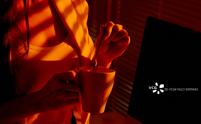 在温暖的办公室灯光下，女人正在搅拌杯中的饮料图片素材