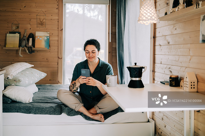 女人在小房子里用智能手机放松，享受咖啡图片素材