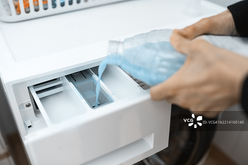 女性的手在洗衣机中手动添加柔顺剂，特写镜头展示她准备洗衣机以开始洗衣服。图片素材