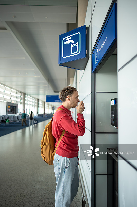 男子在饮水站用锥形杯喝水。公共区域提供免费饮水，热水可用于泡面饮品。图片素材