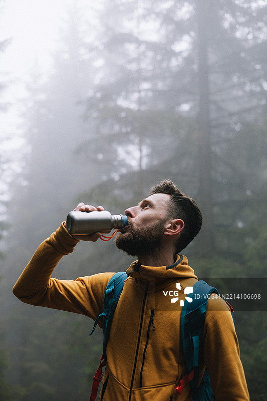 帅气的男人在雾气弥漫的森林中喝水。图片素材