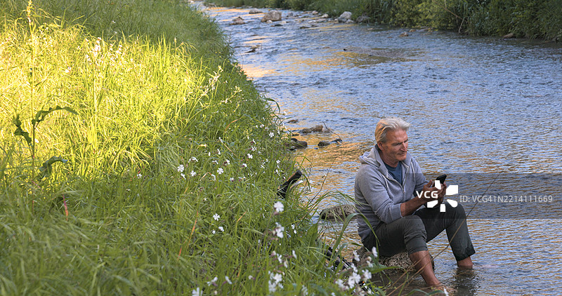 成熟男性在河中使用手机图片素材