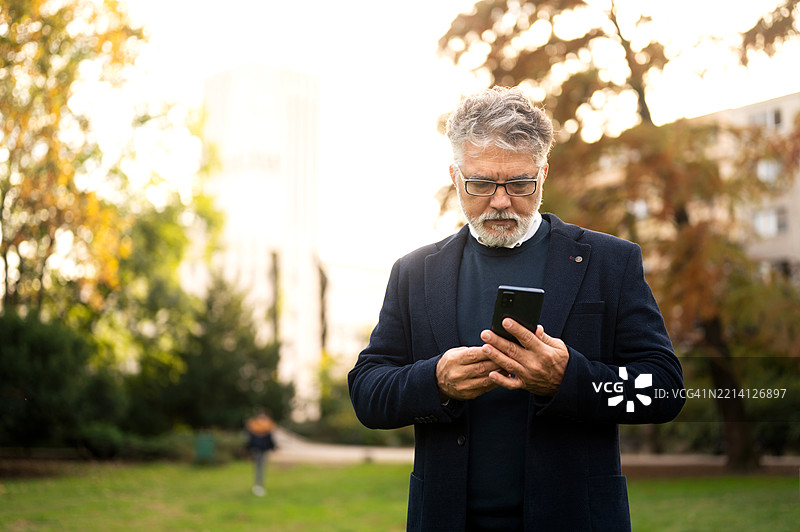 成熟的成年男性在自然公园通过智能手机进行压力对话图片素材