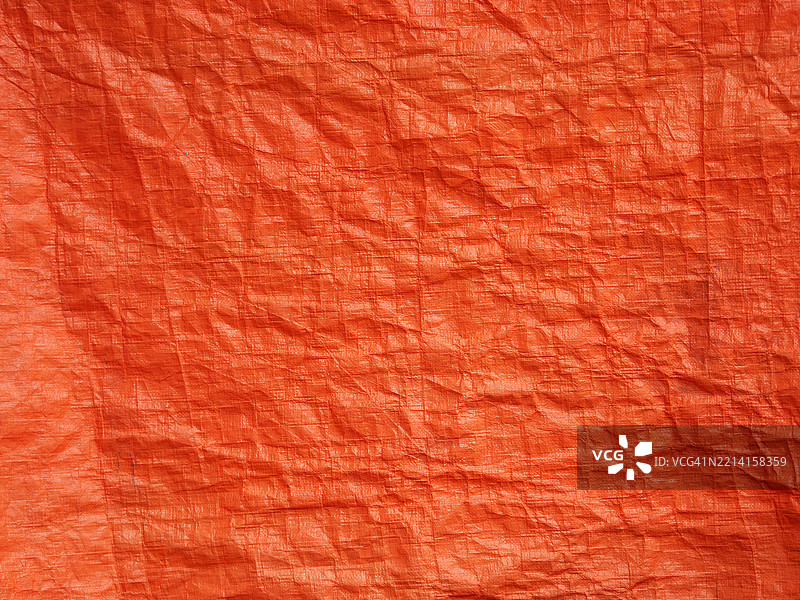 一块橙色、皱褶且波浪状的塑料防水布。粗糙的质感。阳光。自然色彩。法国，上萨瓦省，埃维昂-莱-班。图片素材