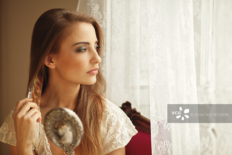 年轻女性在窗边梳理她的长发图片素材