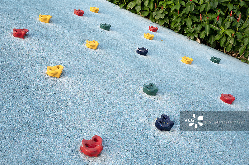 一个蓝色的墙壁上装满了五颜六色的攀爬把手，位于游乐场的攀爬山上图片素材