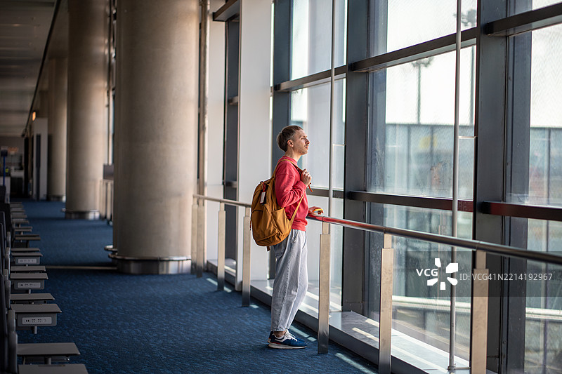深思的独自旅行者透过机场航站楼的窗户凝视。背包客，前方有航班。图片素材