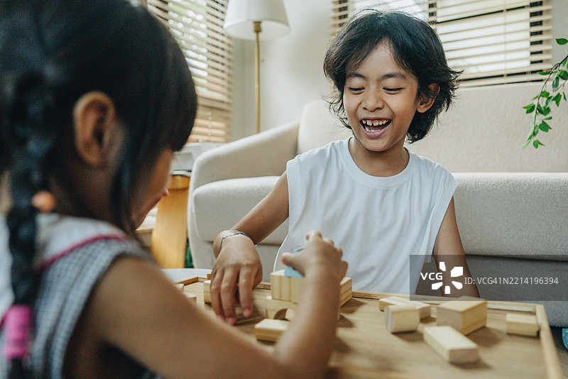 亚洲兄弟姐妹在白天的房间里玩耍。哥哥帮助弟弟搭建玩具房子。童年和纯真的概念。图片素材