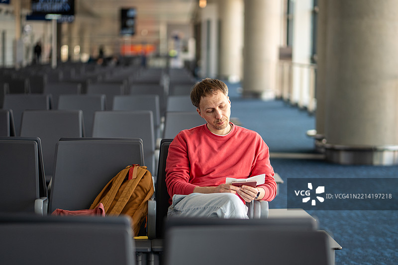 担心的疲惫男子在空荡荡的机场休息室检查旅行文件。长途旅行中的航班问题。图片素材