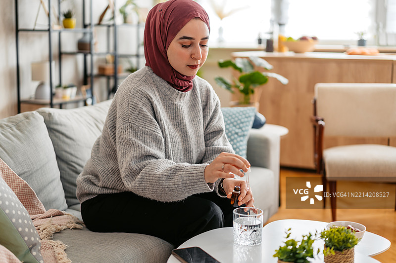 年轻穆斯林女性将药水滴入一杯水中图片素材