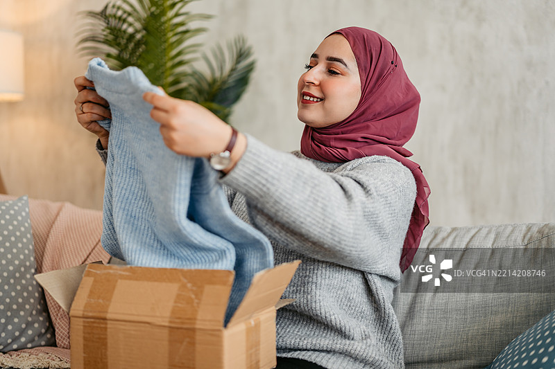 年轻穆斯林女性正在拆包裹，里面是她在线订购的新毛衣图片素材