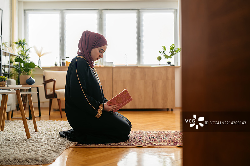 年轻穆斯林女性在家中祈祷垫上阅读《古兰经》图片素材