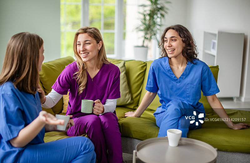 年轻的医疗专业人员在现代休息区享受休息，穿着医务工作服。图片素材