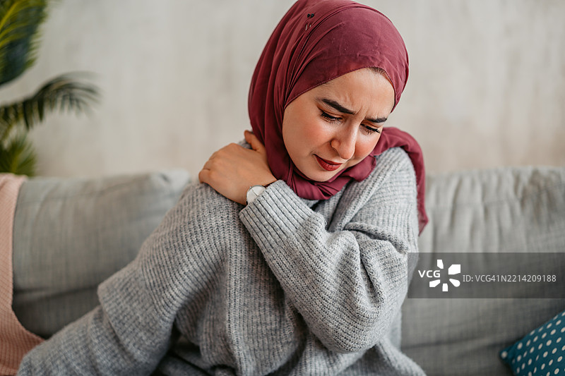 年轻穆斯林女性在家中感到肩部疼痛图片素材