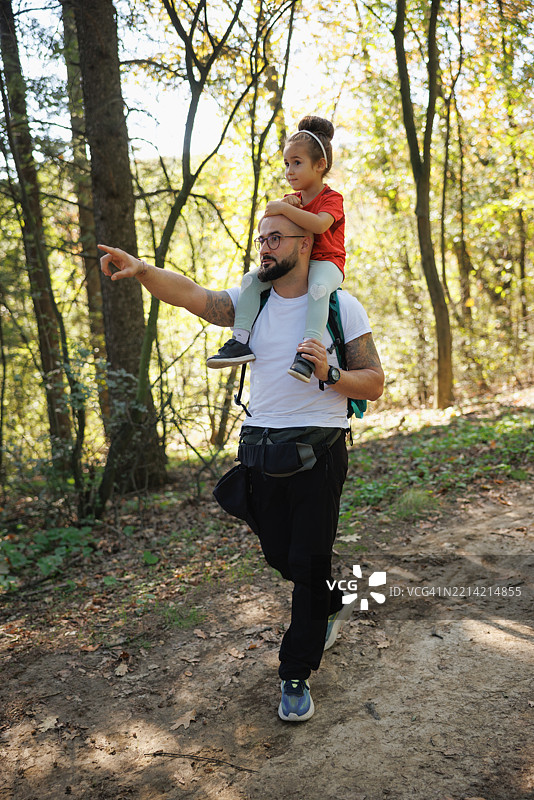 男人在美丽的日子里，肩上扛着他的小女儿，在森林中指向天空。图片素材