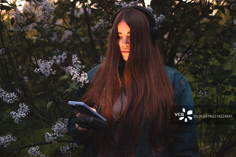 年轻女性在春季傍晚使用智能手机，同时听着个人卡带播放器里的音乐图片素材