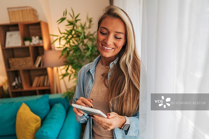年轻女性在家中站在窗边使用平板电脑图片素材