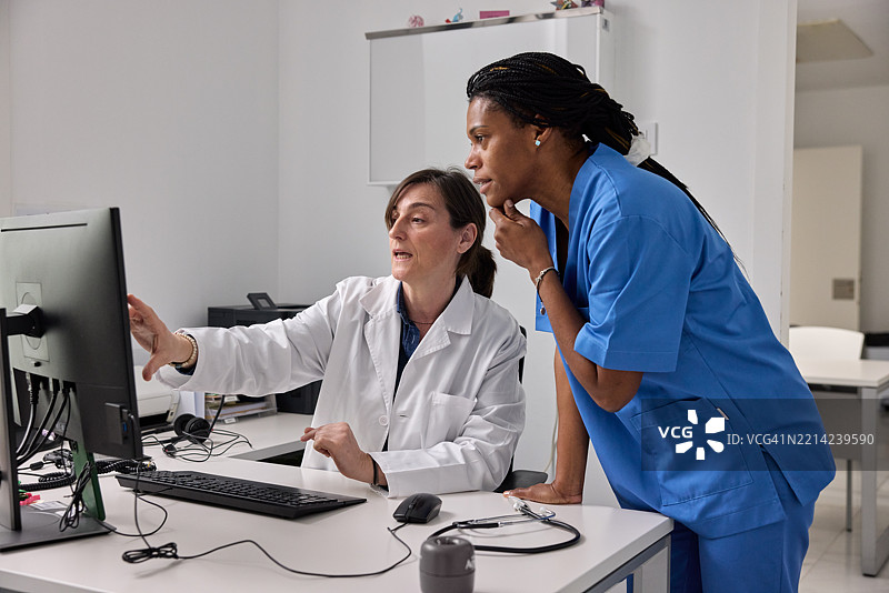 一位医生和一位护士聚集在办公室，坐在电脑前。图片素材