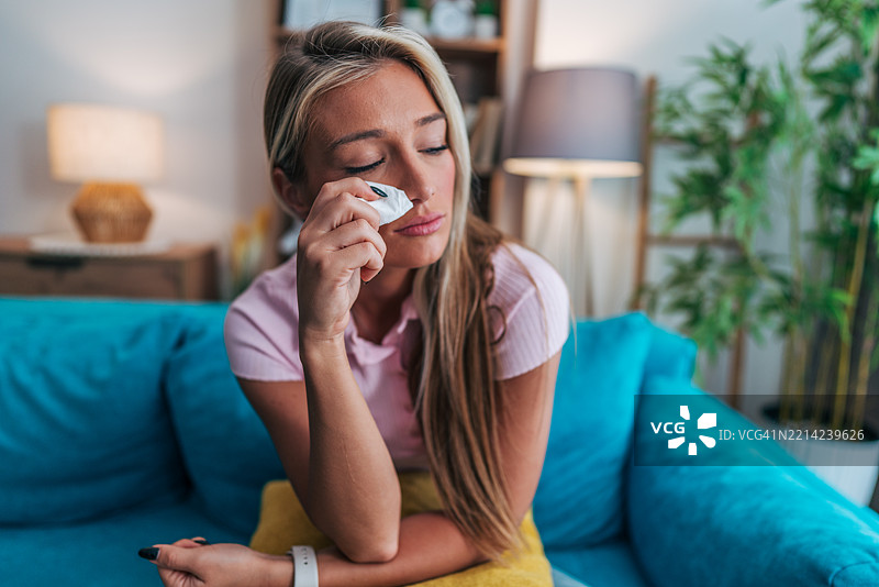 伤心的年轻女性在家沙发上擦拭眼泪图片素材