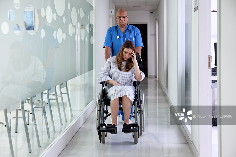 一名护士推着坐在轮椅上的病人沿走廊前行。图片素材