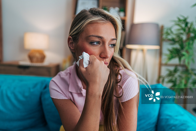伤心的年轻女性在家沙发上擦拭眼泪图片素材