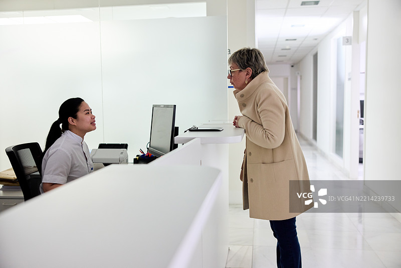 一位女性走到前台接待员那里询问方向。图片素材