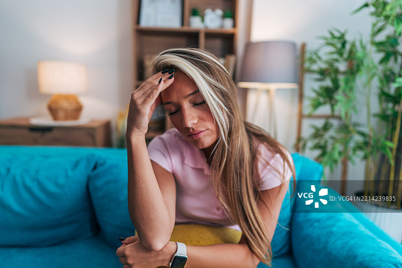 年轻女性坐在家里的沙发上，头痛不已。图片素材