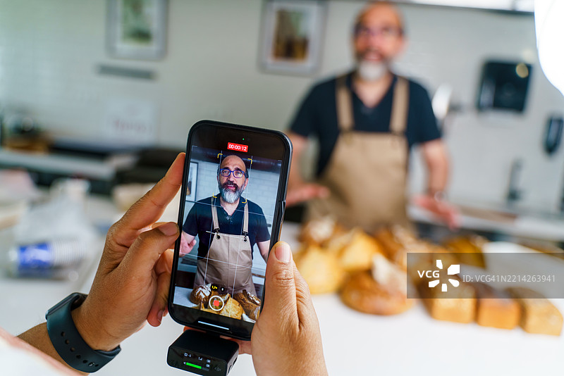 面包师在手工面包店用智能手机拍摄烹饪教程图片素材
