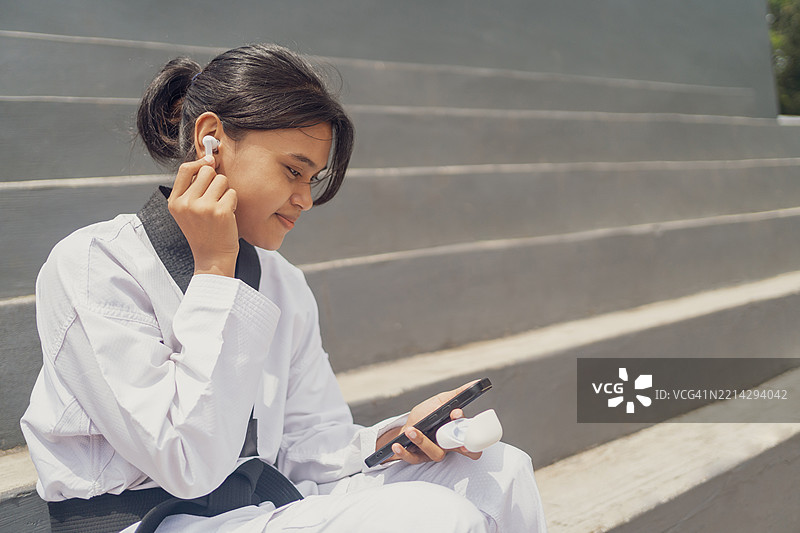 年轻女性跆拳道运动员戴着耳机，正在看她的智能手机图片素材