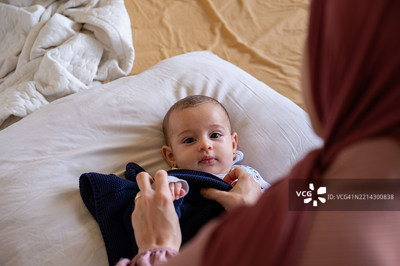 母亲在舒适的床上给宝宝穿衣服图片素材