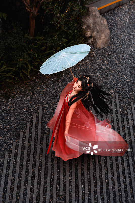 身穿传统服饰的亚洲女性在砾石庭院中旋转着手中的伞。图片素材