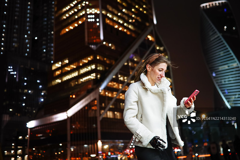 大城市街头的女人在晚上查看她的智能手机屏幕图片素材