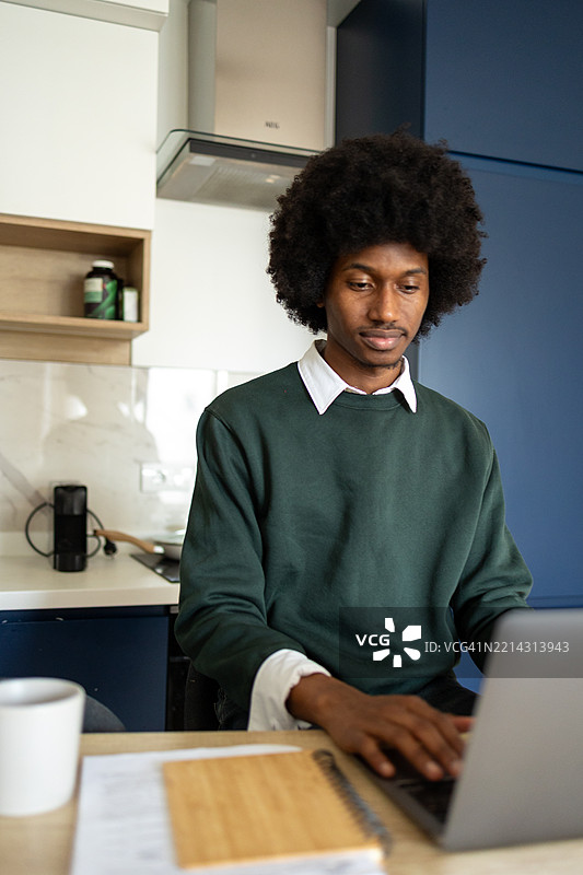 年轻的非裔美国专业人士在现代厨房环境中使用笔记本电脑和文件工作图片素材
