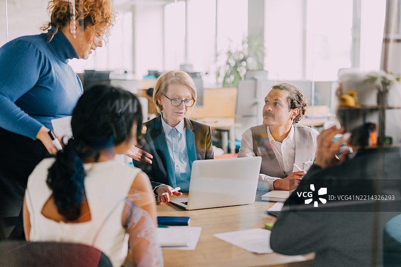 资深女商人在团队会议中查看笔记本电脑上的数据。图片素材